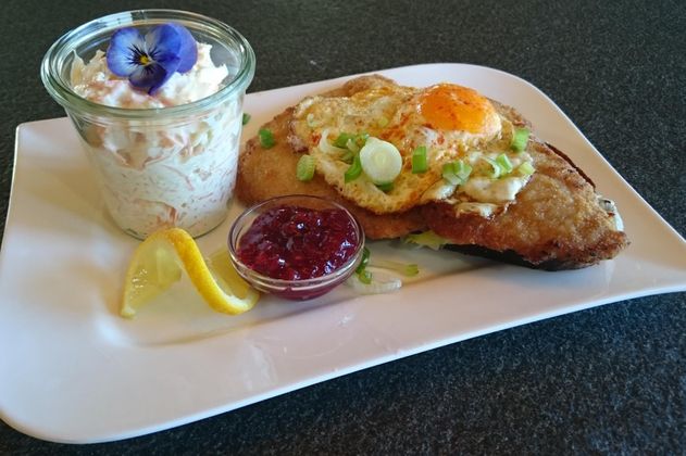 Ein köstliches Gericht mit gebratenem Fisch, Spiegelei und frischem Gemüse. Dazu gibt es einen kleinen Becher mit Joghurt und eine Fruchtsoße.