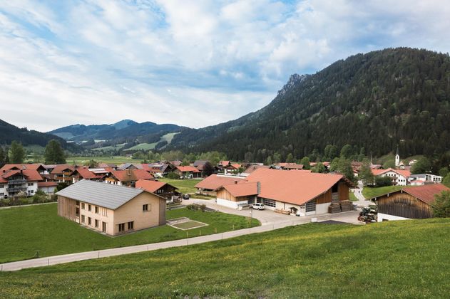 Eine malerische Landschaft mit traditionellen Gebäuden und Bergen im Hintergrund. Die Wiesen sind grün und die Atmosphäre ist friedlich.