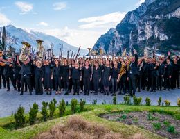 Im Bild ist die Stadtkapelle Memmingen zu sehen mit ihren Instrumenten in der Hand und dem Gebirge im Hintergrund