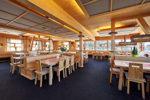 Ein modernes Restaurant mit Holzdekor und großen Fenstern. Die Tische und Stühle sind aus hellem Holz und bieten Platz zum Essen und Entspannen.