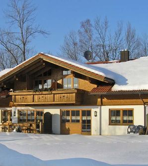 Ein charmantes, holzverkleidetes Haus im Schnee. Die Umgebung ist ruhig und winterlich mit kahlen Bäumen.
