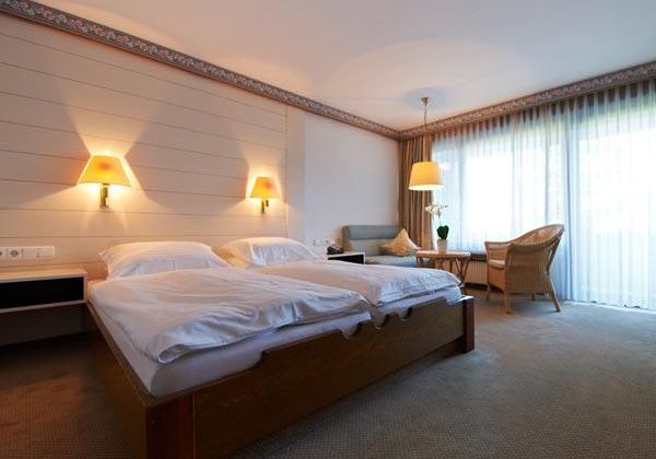 Ein komfortables Schlafzimmer mit zwei Betten und sanften Hängeleuchten. Große Fenster sorgen für viel Tageslicht und eine gemütliche Atmosphäre.