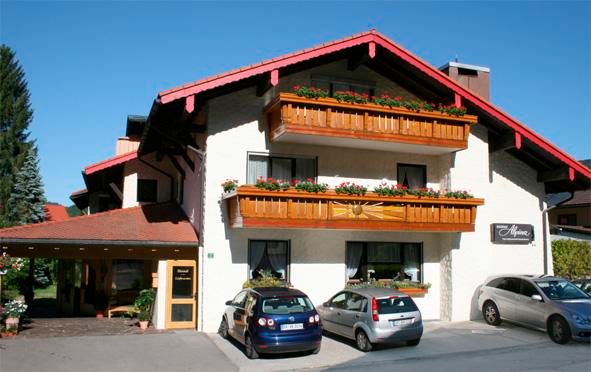 Ein charmantes Gebäude mit traditioneller Architektur und blühenden Balkonen. Vor dem Haus stehen mehrere Autos geparkt.