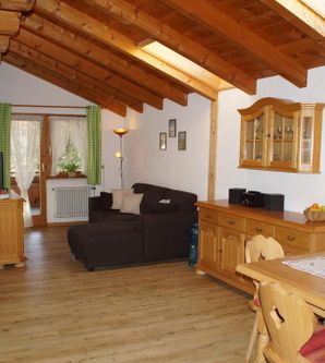 Ein gemütliches Wohn- und Esszimmer mit Holzdecke und großen Fenstern. Die Möbel sind aus hellem Holz, und es gibt einen komfortablen Sofa und einen Esstisch.