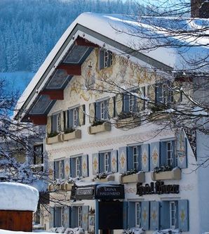 Ein charmantes, verschneites Hotel mit traditioneller Fassade und farbenfrohen Fensterläden. Umgeben von einer malerischen Winterlandschaft.
