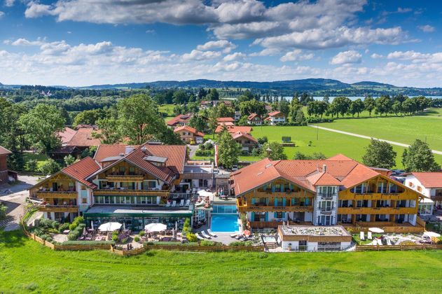 Ein malerisches Resort mit roten Dächern und einem Pool in der Mitte. Umgeben von grünen Wiesen und einem schönen Himmel mit Wolken.