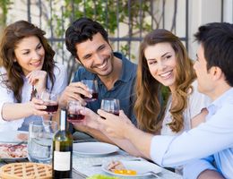 A group of four friends enjoys a joyful meal outdoors. They toast with glasses and laugh together.