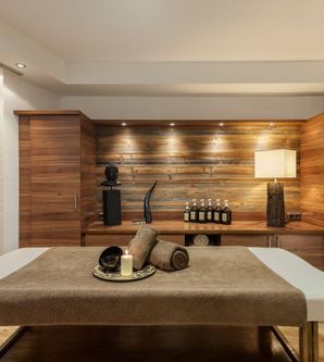 Ein eleganter Wellnessraum mit einem Massagetisch und stilvollen Holzmöbeln. Im Hintergrund stehen dekorative Objekte und entspannende Beleuchtung.