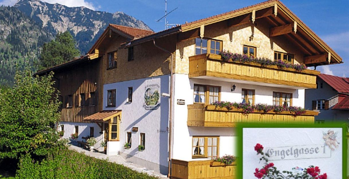 Ein charmantes, traditionelles Haus in den Bergen mit Blumenbalkonen. Die Umgebung ist grün und malerisch, ideal für eine Erholung.