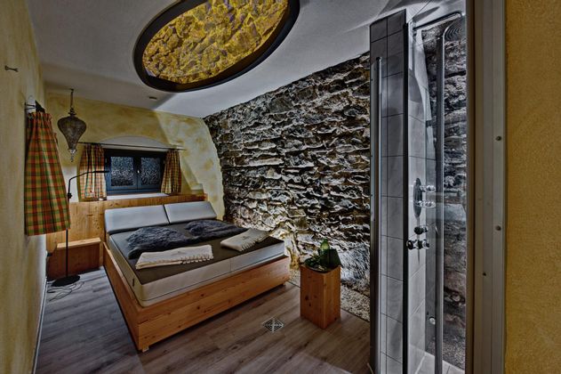 Ein gemütliches Schlafzimmer mit einer Steinwand und einem großen Fenster. Die Einrichtung ist modern, mit einem Doppelbett und einer Dusche in der Ecke.