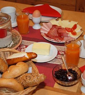 Ein reichhaltiges Frühstück mit frischen Brötchen, Wurst, Käse und Eiern. Dazu gibt es Säfte und Marmelade in schönen Schalen.