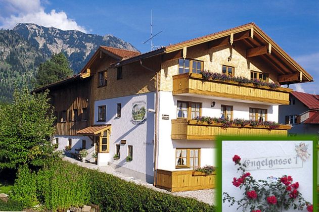 Ein charmantes, traditionelles Haus in den Bergen mit Blumenbalkonen. Die Umgebung ist grün und malerisch, ideal für eine Erholung.