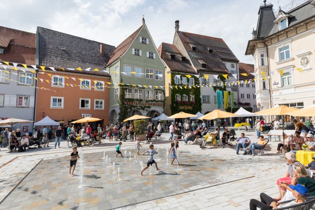 Kinder rennen durchs Wasserspiel auf dem geschmückten, lebendigen Marktplatz, mitten in der Altstadt von Isny. 