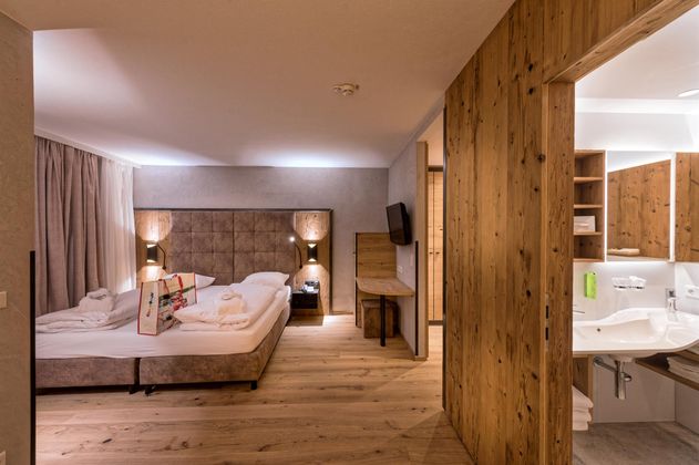 Ein modernes Hotelzimmer mit Holzfußboden und stilvoller Einrichtung. Es gibt ein großes Bett, einen Fernseher und ein angrenzendes Badezimmer.