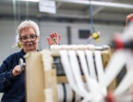 ältere Dame setzt Textilmaschine in Bewegung.