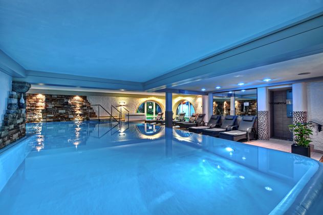 Ein luxuriöser Innenpool mit sanftem blauem Licht und modernen Liegen. Die entspannende Atmosphäre schafft einen perfekten Ort zum Relaxen.