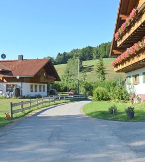 Eine ruhige ländliche Szene mit zwei charmanten Häusern und einem kleinen Weg. Umgeben von grünen Wiesen und sanften Hügeln.