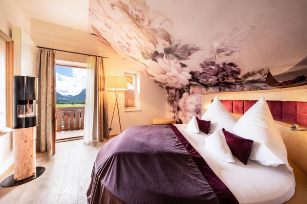 Ein elegantes Zimmer mit einem großen Bett und einer Blumenwandgestaltung. Der Blick aus dem Fenster zeigt eine beeindruckende Berglandschaft.
