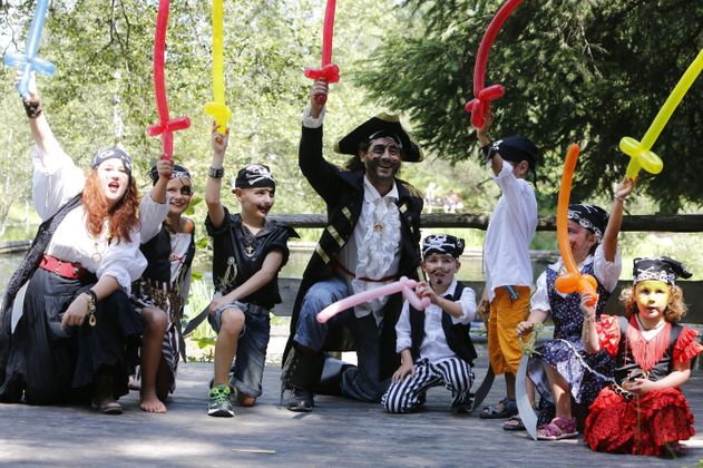 Eine Gruppe verkleideter Piratenfeen feiert im Freien. Sie halten bunte Ballon-Schwerter in die Luft und strahlen vor Freude.