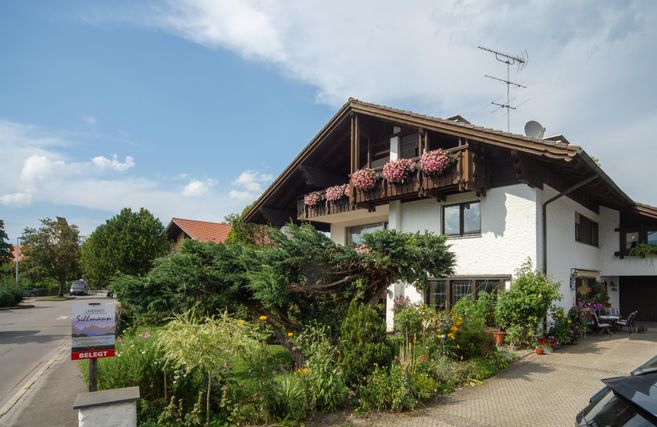 A charming house with a beautiful garden and blooming plants. The sky is clear and it is a sunny day.
