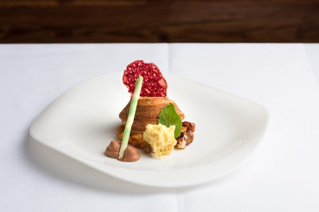 Ein kunstvoll angerichteter Dessertteller mit einer Schicht aus Karamell, einer fruchtigen Dekoration und einer cremigen Beilage. Das Gericht ist auf einem eleganten weißen Teller serviert.