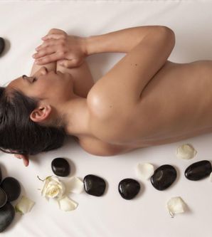 Eine entspannende Spa-Szene mit einer Frau, die auf einer Liege liegt. Um sie herum liegen glatte Steine und Rosenblätter.