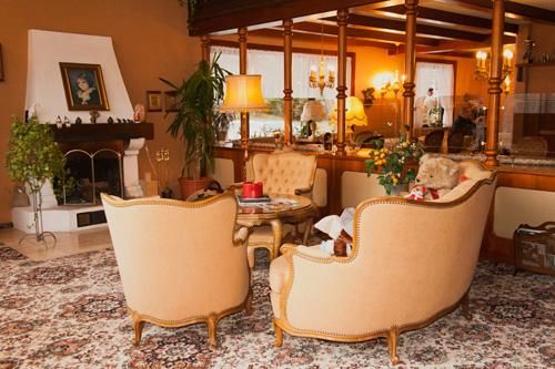Ein gemütliches Wohnzimmer mit beigen, gepolsterten Sesseln und einem eleganten Couchtisch. Im Hintergrund sind Pflanzen und eine offene Küche zu sehen.