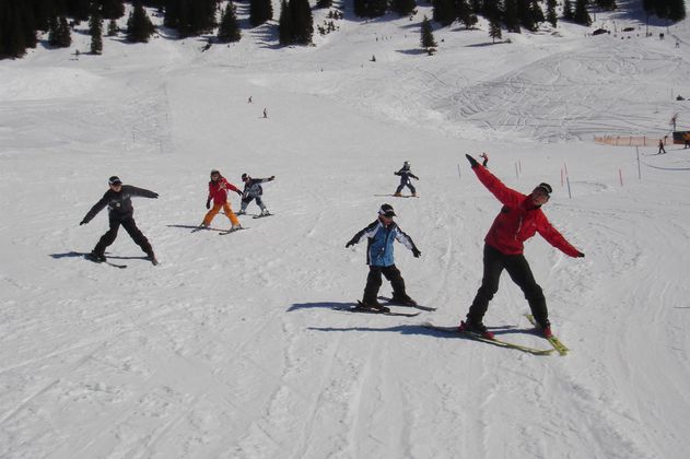 Skigruppe auf breiter, verschneiter Piste. Sechs Personen in bunten Skianzügen.