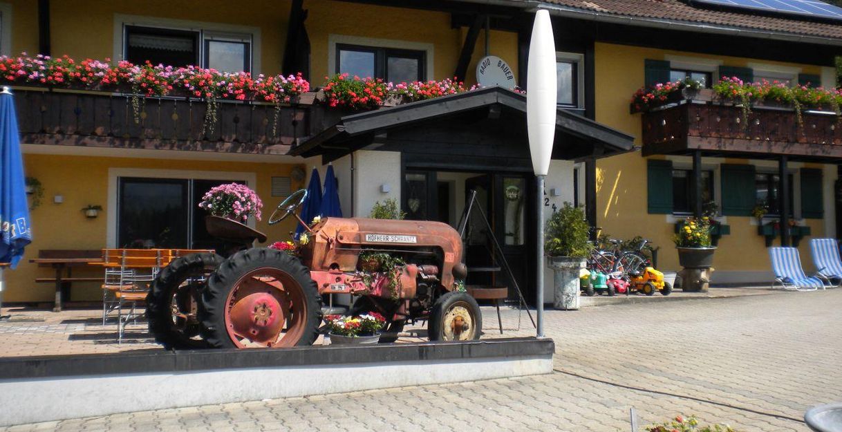 Ein roter Oldtimer-Traktor steht vor einem gelben Gebäude mit Blumenkästen. Das Haus hat Balkone und eine einladende Atmosphäre.