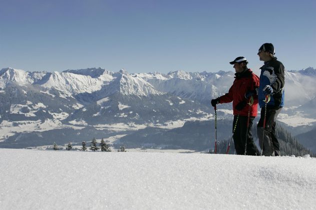 Zwei Männer mit Skitourenausrüstung stehen auf einer verschneiten Anhöhe.