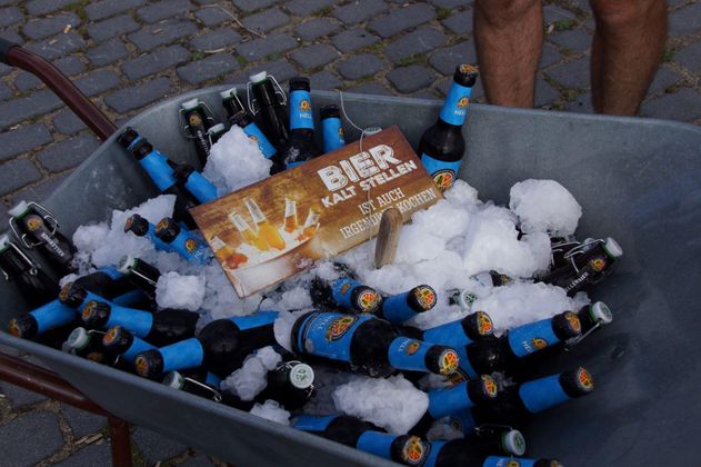Eine Schubkarre voller Bierflaschen und Eiswürfeln. Darauf liegt ein Schild mit der Aufschrift "BIER KAUFEN".
