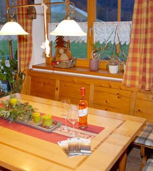 Ein gemütlicher Essbereich mit einem Holztisch, dekoriert mit einer Tischdecke und einer Vase. Auf dem Tisch stehen eine Flasche Rosewein und Gläser.