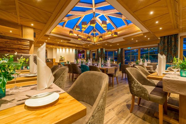 Ein elegantes Restaurant mit gemütlichen Tischen und Stühlen. Das Licht strömt durch das Glasdach und schafft eine einladende Atmosphäre.