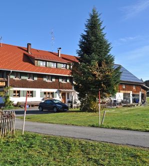 Ein traditionelles Bauernhaus mit rotem Dach und schönen Holzelementen. Umgeben von einer grünen Landschaft und einem klaren Himmel.