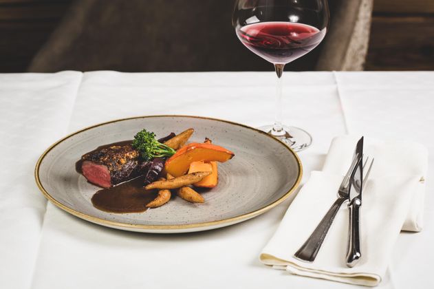 Ein köstliches Gericht mit Rindersteak, buntem Gemüse und einer Sauce. Dazu steht ein Glas Rotwein auf dem Tisch.