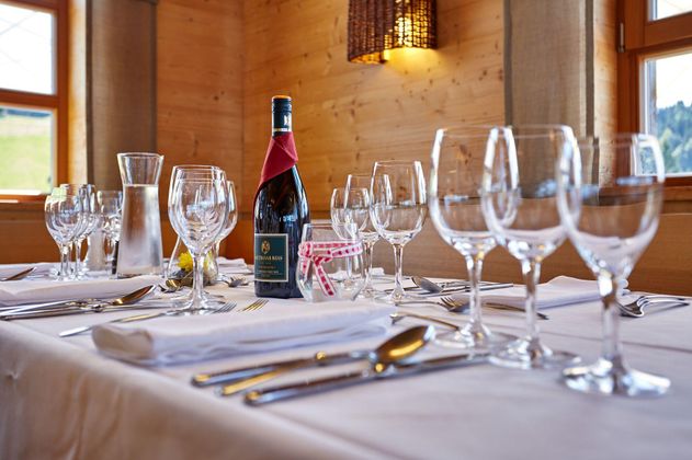 Ein elegantes Tischarrangement mit Gläsern, Besteck und einer Flasche Wein. Die Atmosphäre ist gemütlich und einladend.