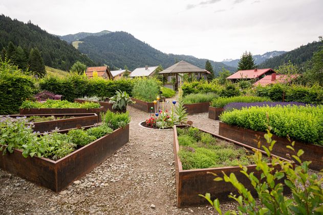 Kräutergarten mit Hochbeeten, Kieswegen, bunten Glasobjekten.