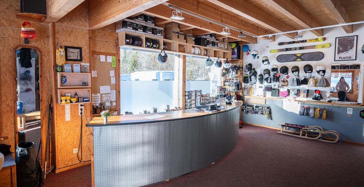 Innenansicht Planet B Wintersport: Theke, Regale mit Helmen, Schuhen, Boards. Schlitten, Stöcke. Helle Beleuchtung, Holzbalken.