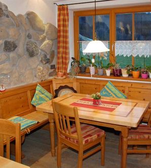 Eine gemütliche Küche mit einem Holztisch und Sitzbank. Am Fenster stehen viele Pflanzen und die Wände sind mit Steinen dekoriert.