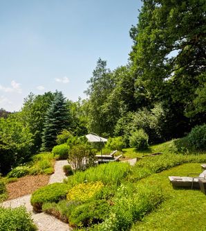 Ein schöner Garten mit gepflegten Pflanzen und Sitzgelegenheiten. Im Hintergrund sind niedrige Berge und ein blauer Himmel zu sehen.
