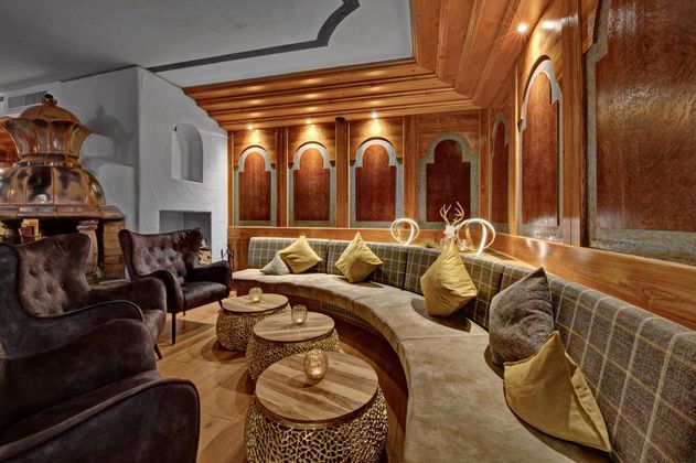 Ein stilvolles Lounge-Interieur mit bequemen Sesseln und einem geschwungenen Sitzbereich. Warmes Licht und dekorative Kissen sorgen für eine entspannte Atmosphäre.
