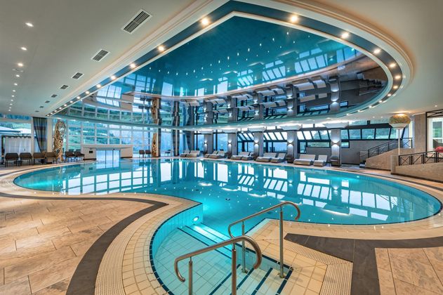 Ein eleganter Innenpool mit klarem Wasser und modernen Liegen. Die große Fensterfront sorgt für viel natürliches Licht und eine entspannende Atmosphäre.