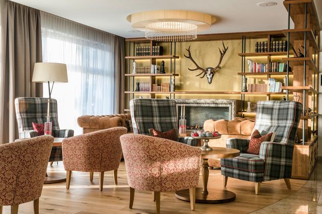 Ein eleganter Wohnraum mit bequemen Sessel und stylischen Regalen. Ein beeindruckendes Geweih dekoriert die Wand über dem Kamin.