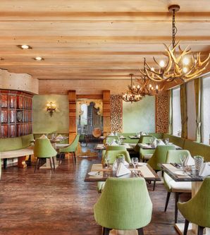 Ein modernes Restaurant mit Holzmöbeln und grünen Stühlen. Die Einrichtung ist stilvoll und einladend mit vielen Fenstern und schönem Licht.