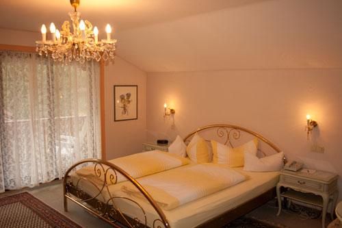 Ein elegantes Schlafzimmer mit einem großen Doppelbett und goldenen Akzenten. Eine Kristallleuchte und sanftes Licht schaffen eine gemütliche Atmosphäre.