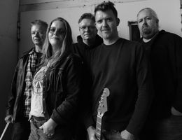 Schwarz-weiß-Bild der fünf Mitglieder mit Gitarre posierend vor einer Wand.