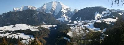 Eine beeindruckende Winterlandschaft mit schneebedeckten Bergen und grünen Tälern. Der klare Himmel ergänzt die malerische Aussicht.