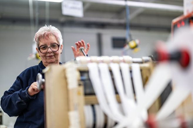ältere Dame setzt Textilmaschine in Bewegung.