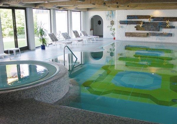 Ein eleganter Innenpoolbereich mit bequemen Liegen und großen Fenstern. Das Wasser reflektiert beruhigende Farben und schafft eine entspannende Atmosphäre.