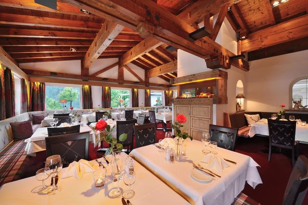Ein elegantes Restaurant mit rustikalen Holzbalken und schön eingedeckten Tischen. Große Fenster bieten einen Blick auf die Umgebung.